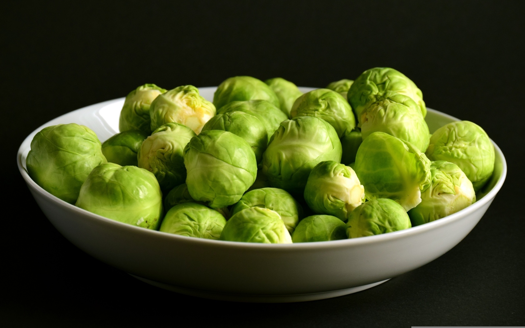 Зеленая брюссельская капуста в тарелке на черном фоне