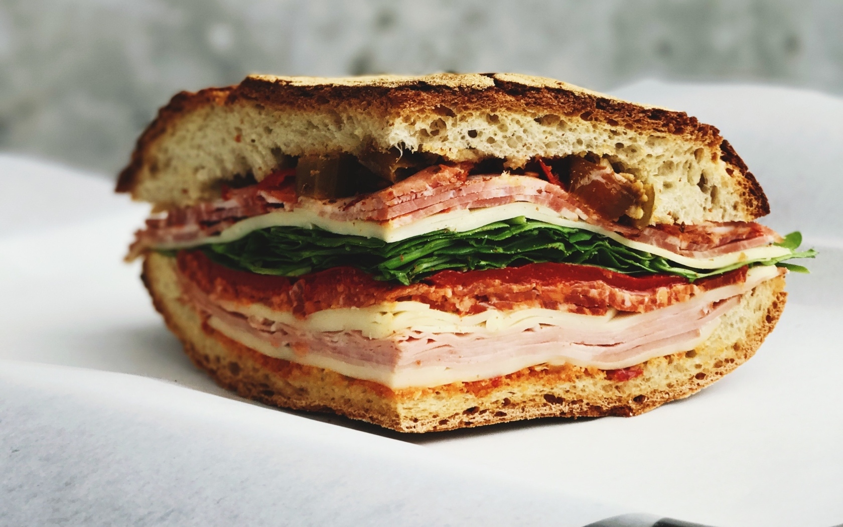 Кусок булки с колбасой, ветчиной и листьями салата