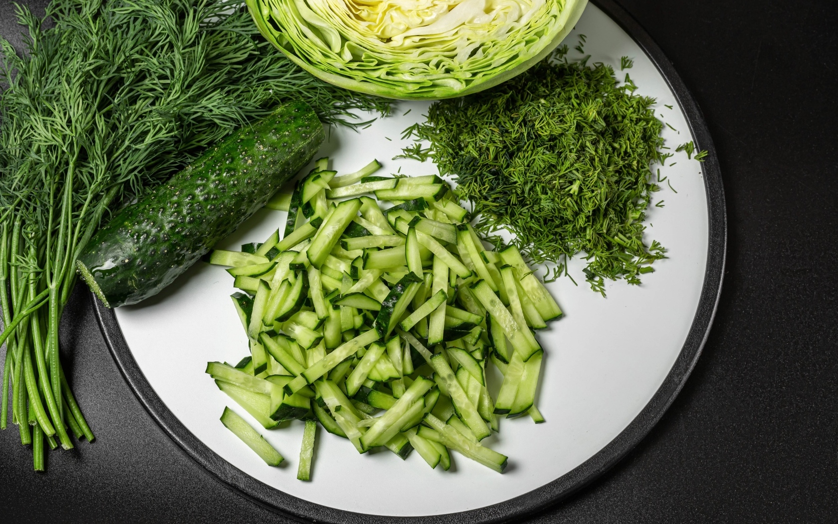 Нарезанные огурцы на столе с капустой и укропом