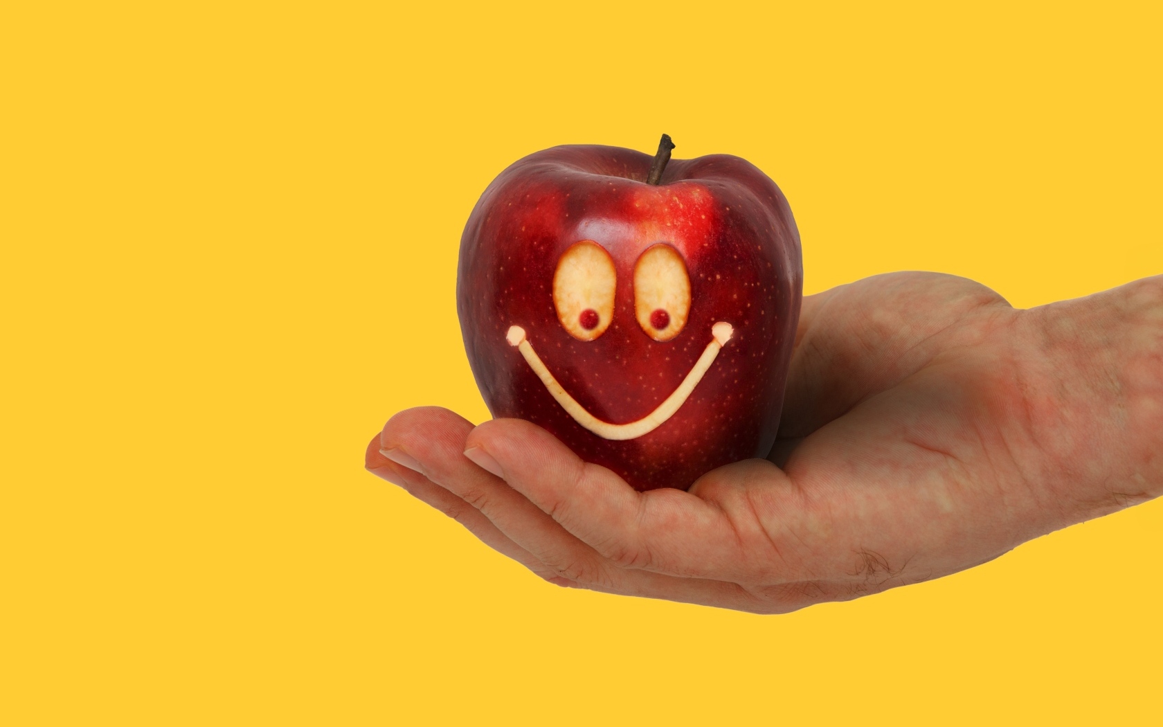 Яблоко на ладони на желтом фоне