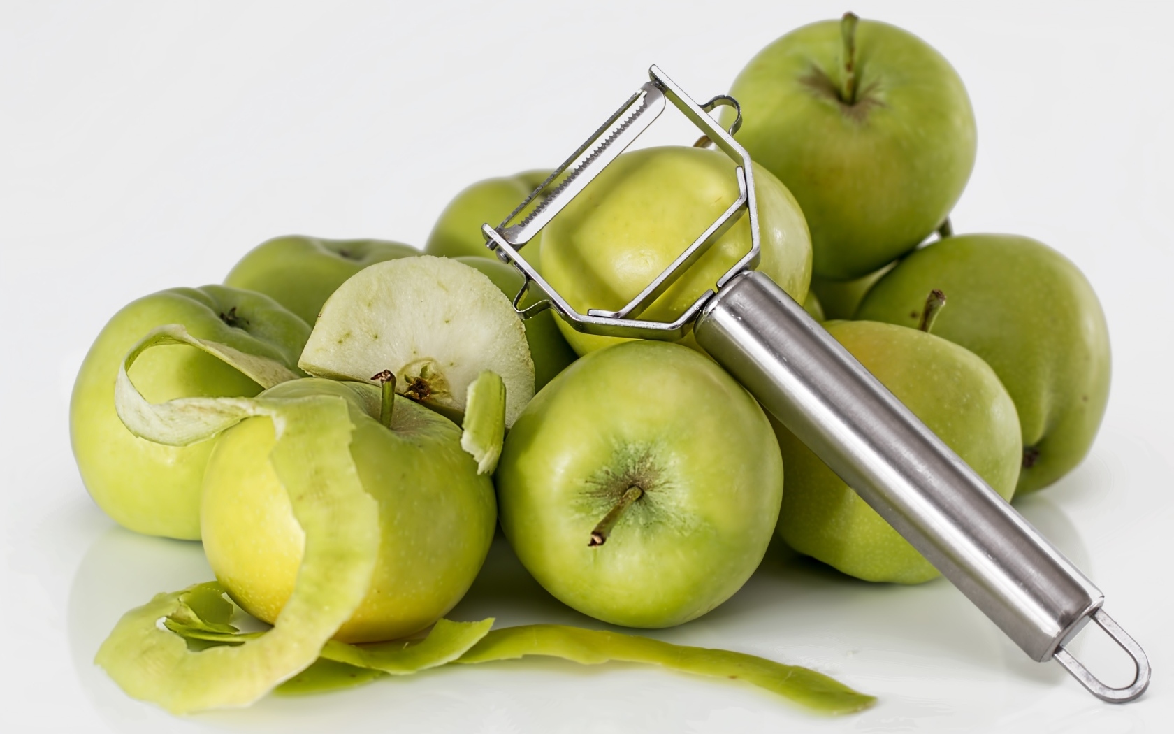 Зеленые яблоки с овощечисткой на белом фоне