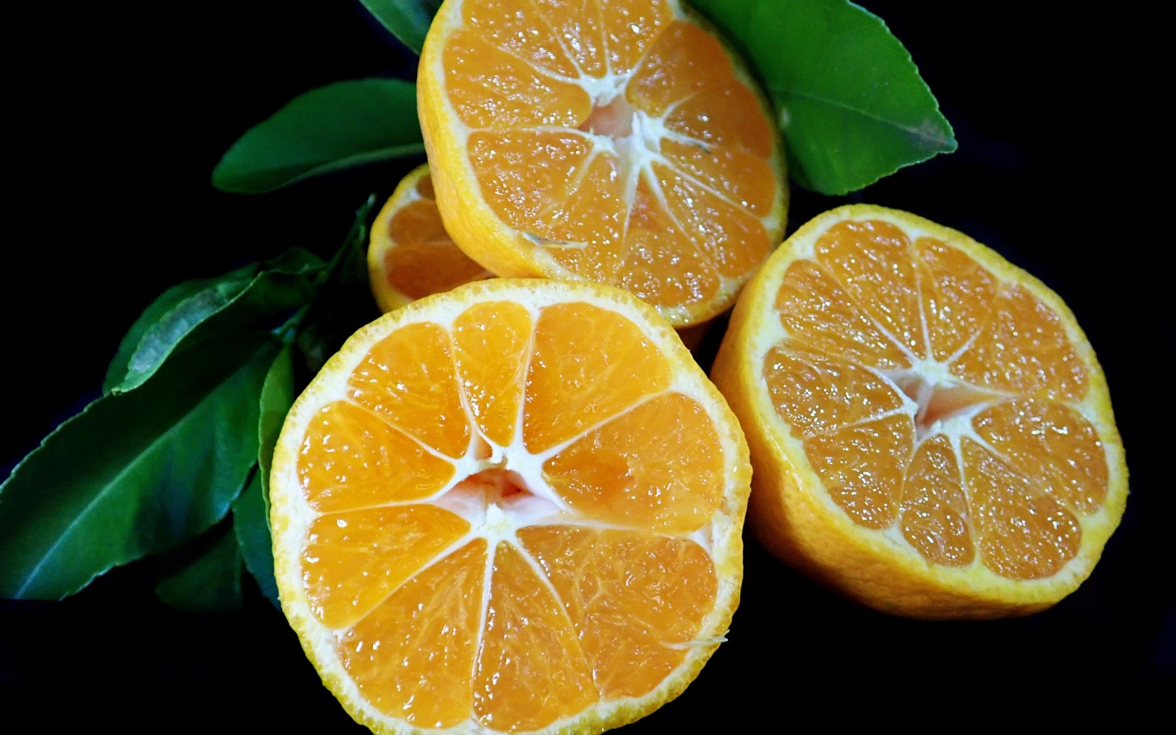 Половинки мандарина с зелеными листьями на черном фоне