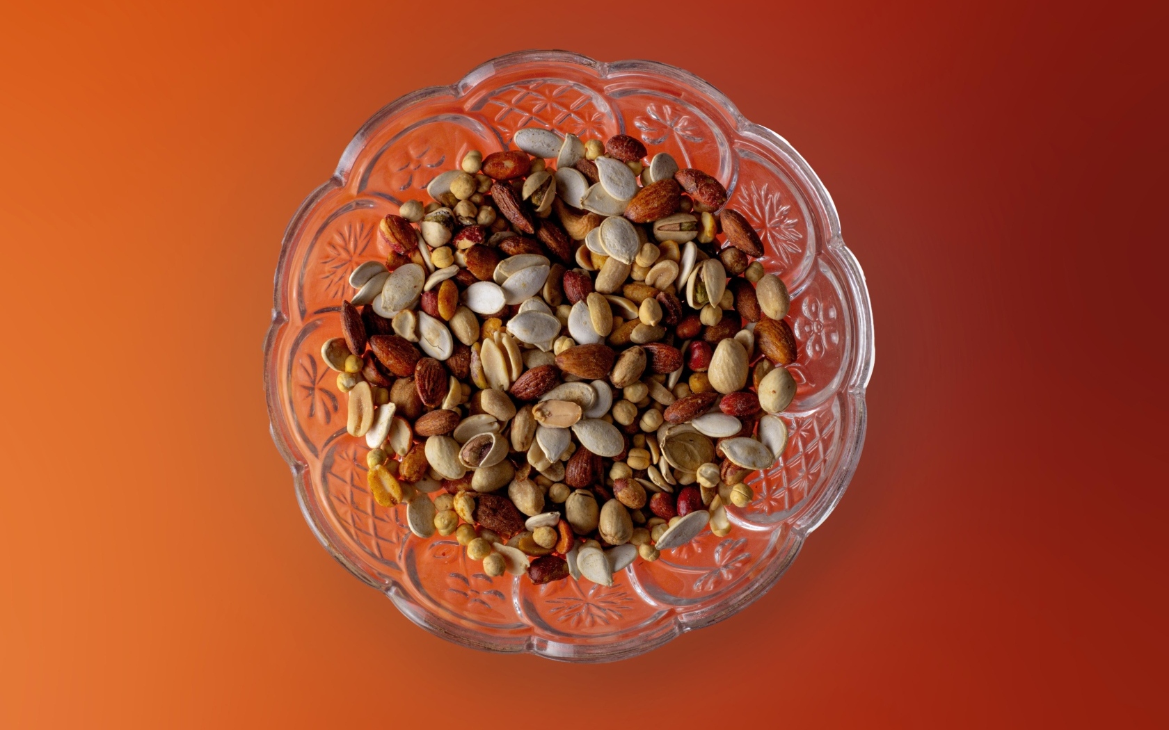 Разные орехи в стеклянной посуде на оранжевом фоне