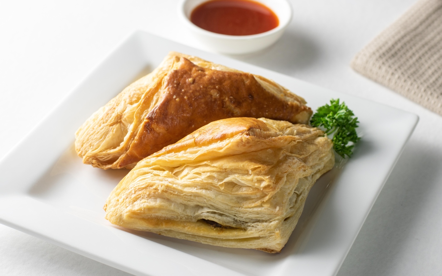 Слоеная выпечка на белой тарелке с соусом