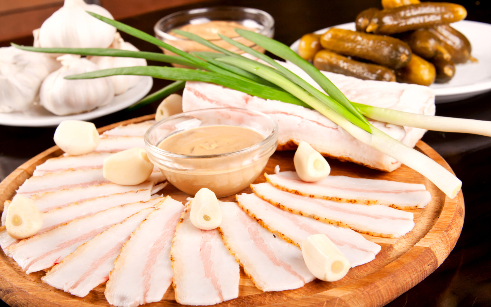 Нарезанное сало с чесноком и солеными огурцами на столе