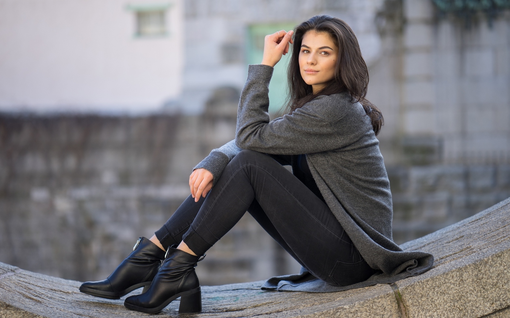 Милая девушка в сером наряде сидит на бетонной плите