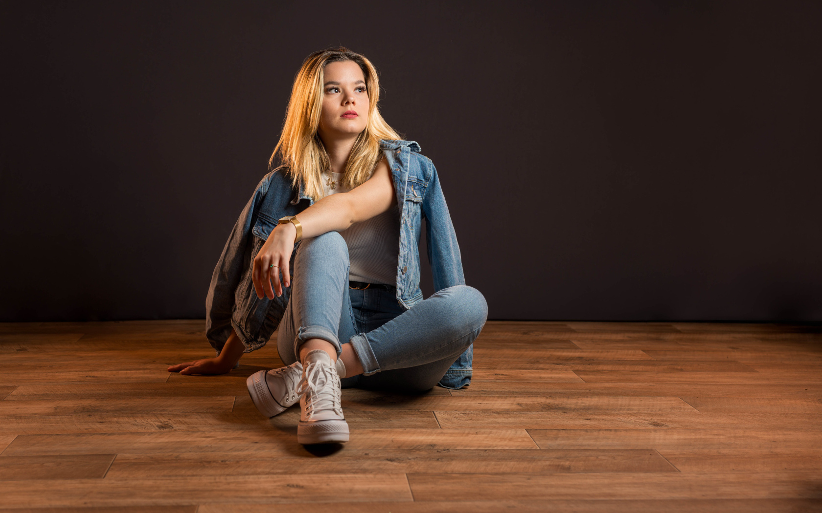 Девушка в джинсовом костюме сидит на полу