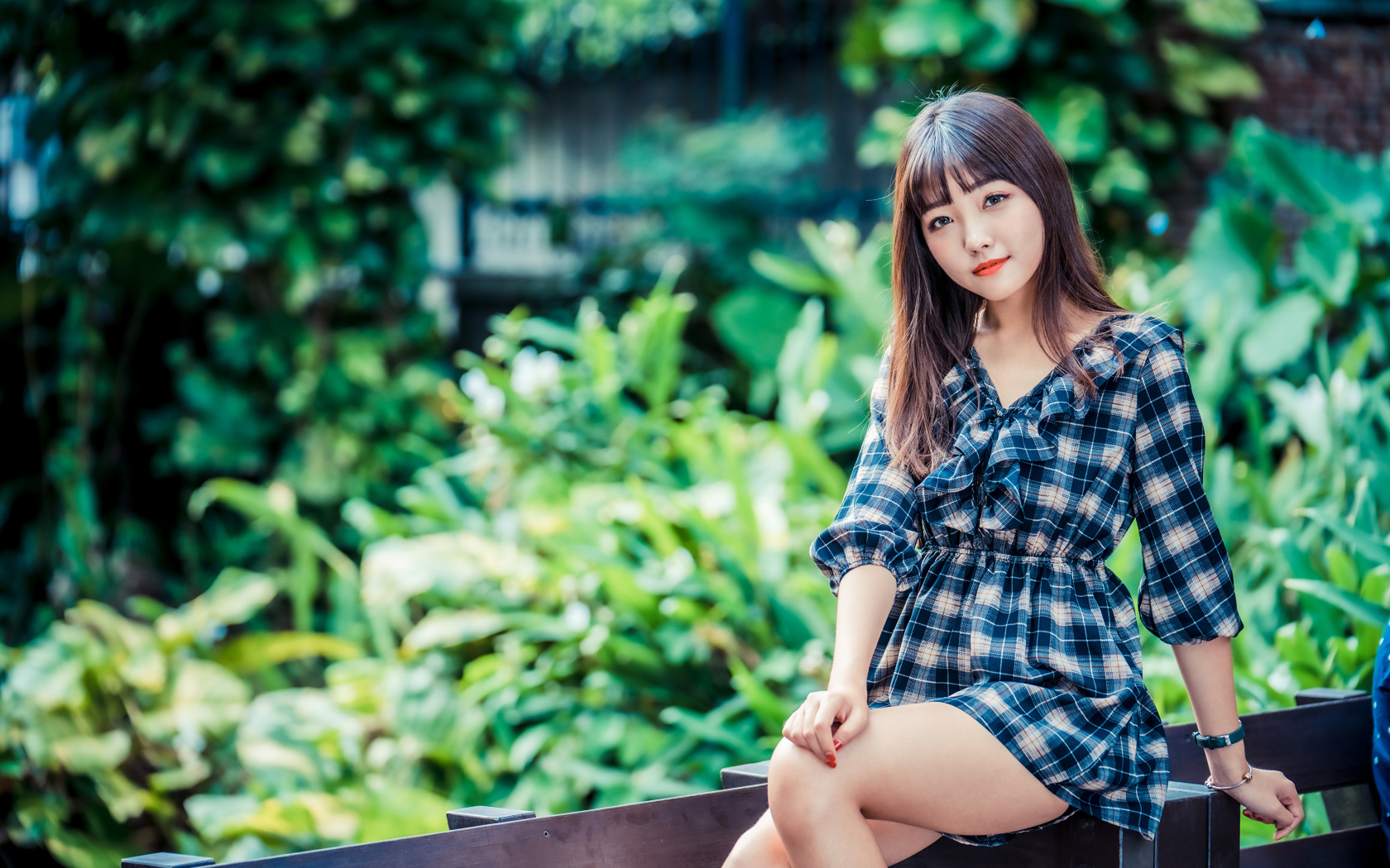 Молодая девушка в клетчатом платье сидит на заборе