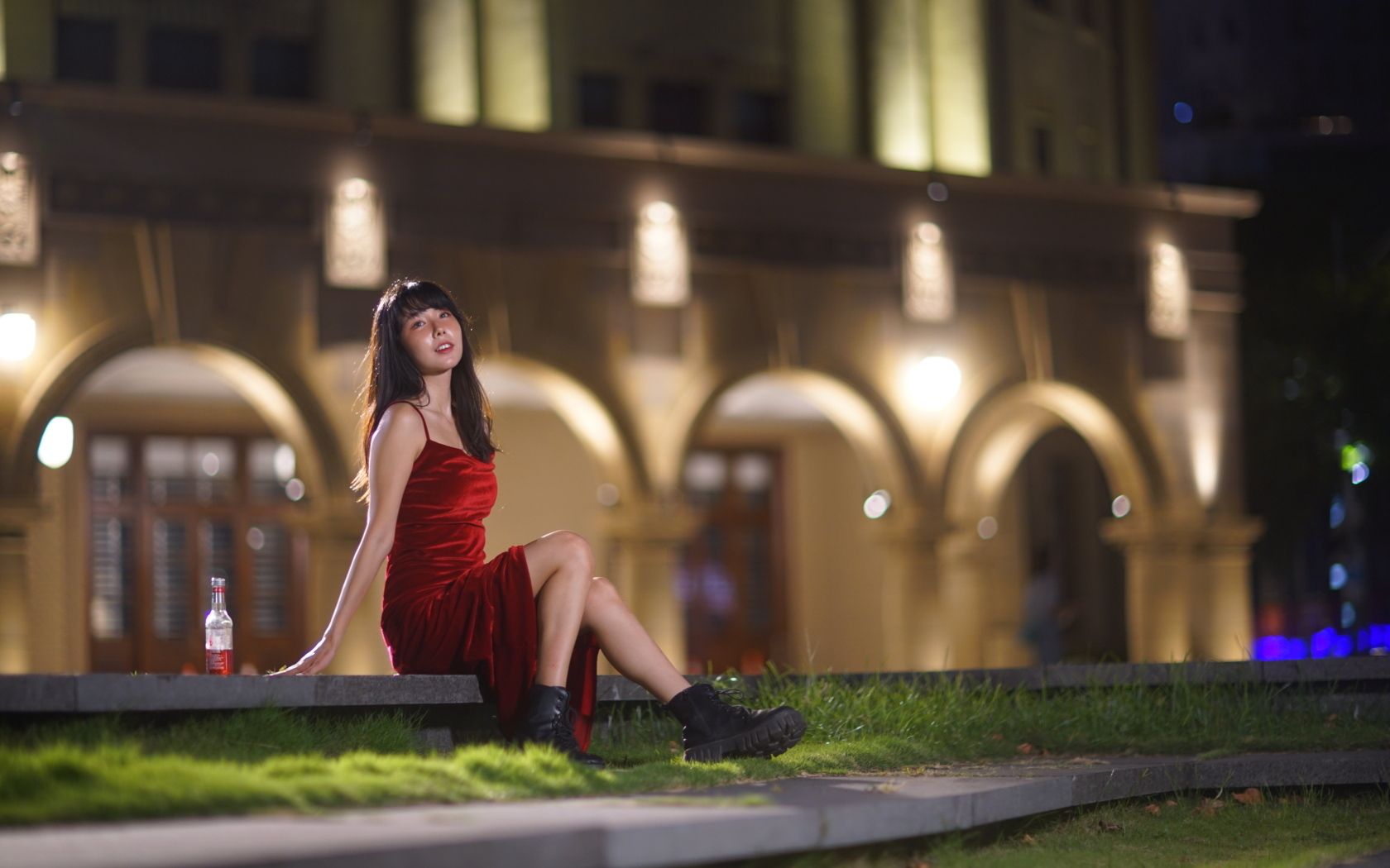 Азиатка в длинном красном платье сидит на ступенях