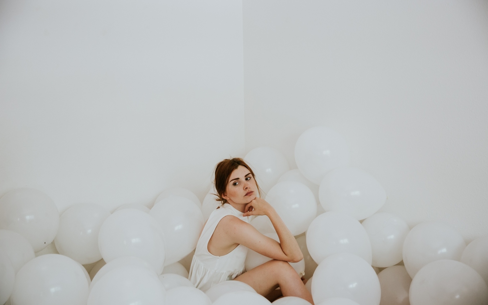Грустная девушка сидит в белых воздушных шариках