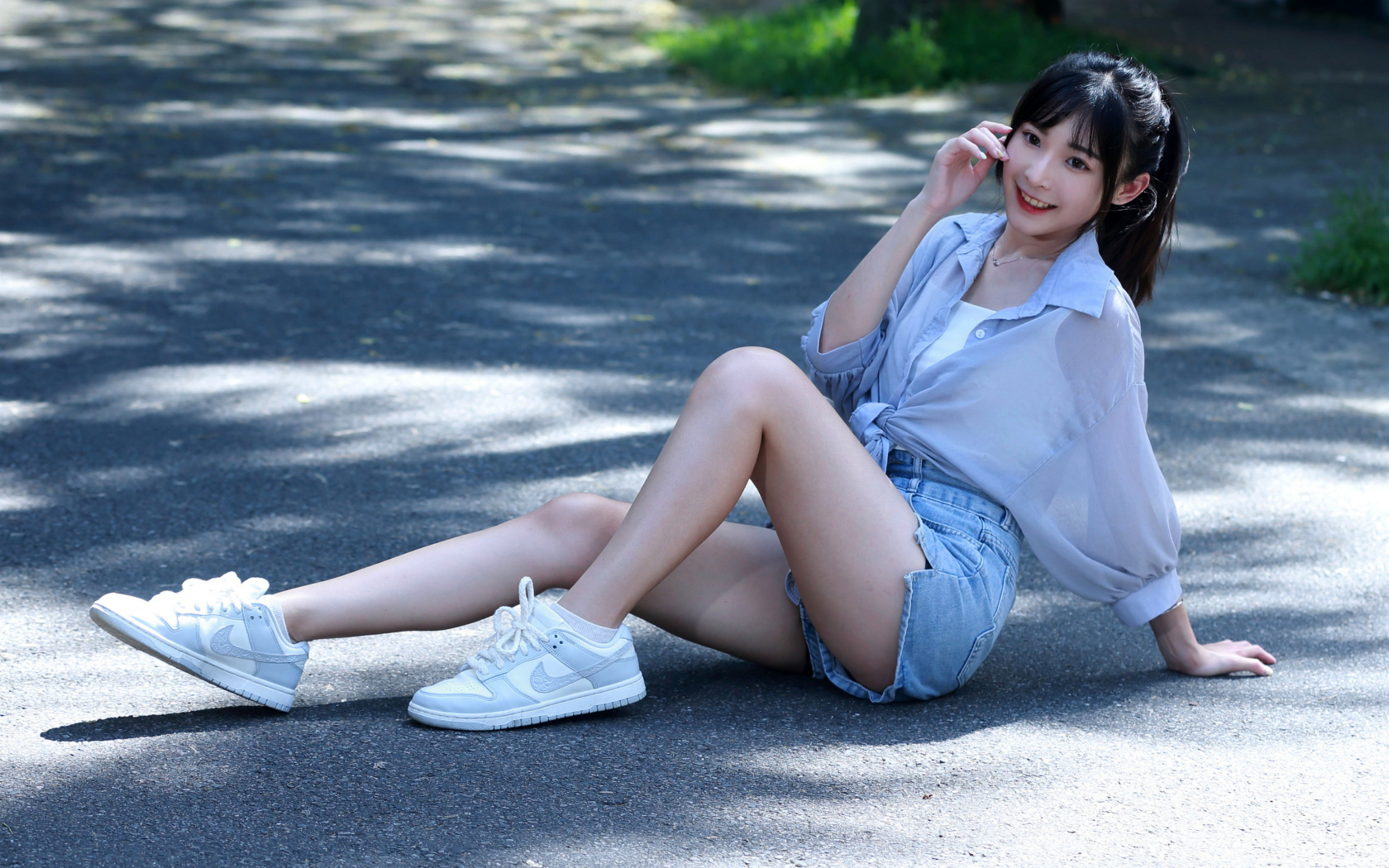 Улыбающаяся девушка азиатка в кедах сидит на дороге