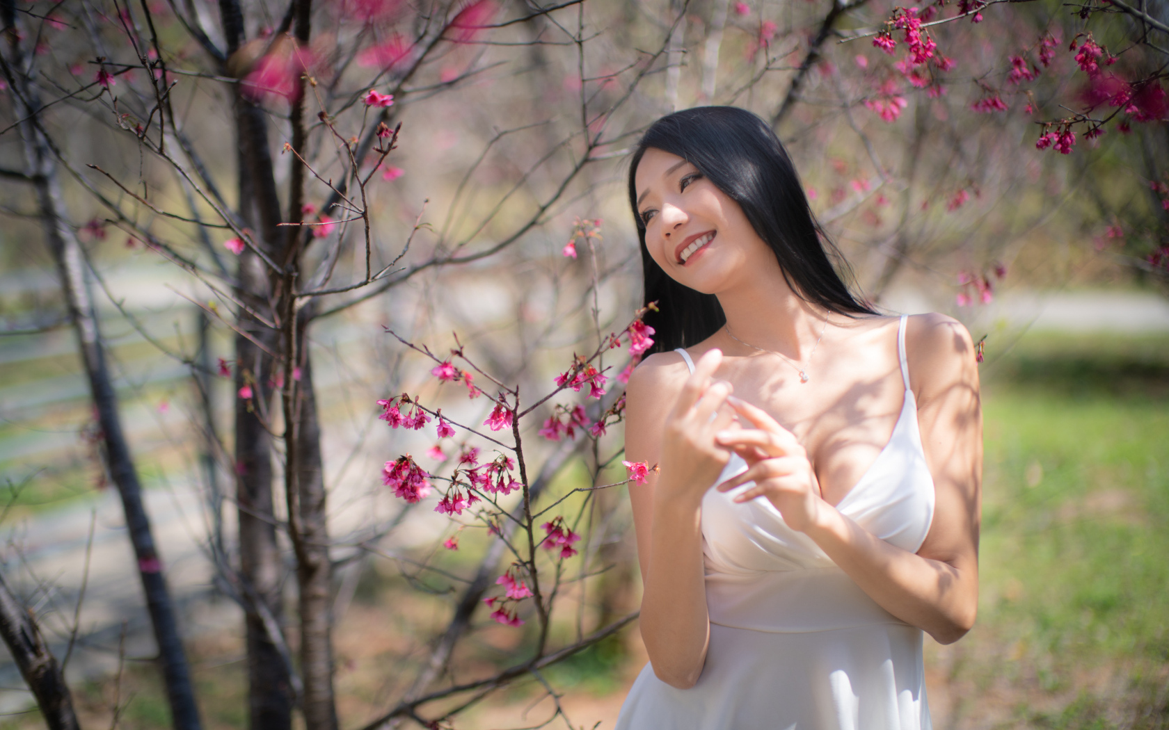 Улыбающаяся девушка в белом платье у дерева с цветами