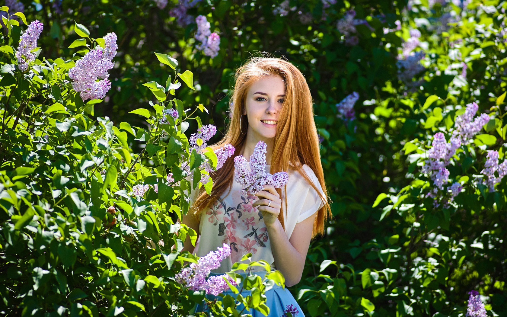 Улыбающаяся девушка стоит у куста сирени