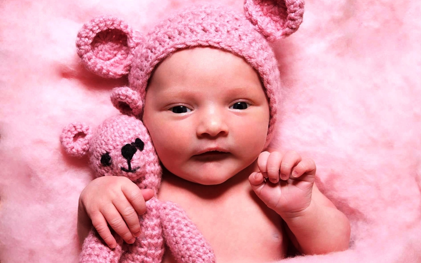 Грудной ребенок в розовой шапке с игрушкой в руке