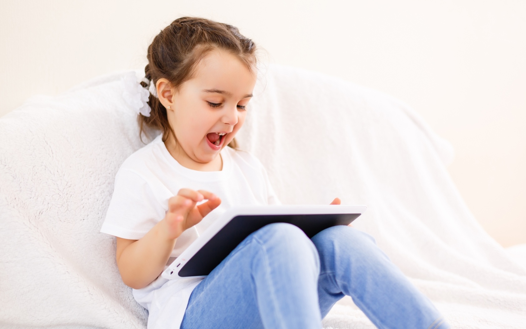 Веселая девочка с планшетом на кровати 