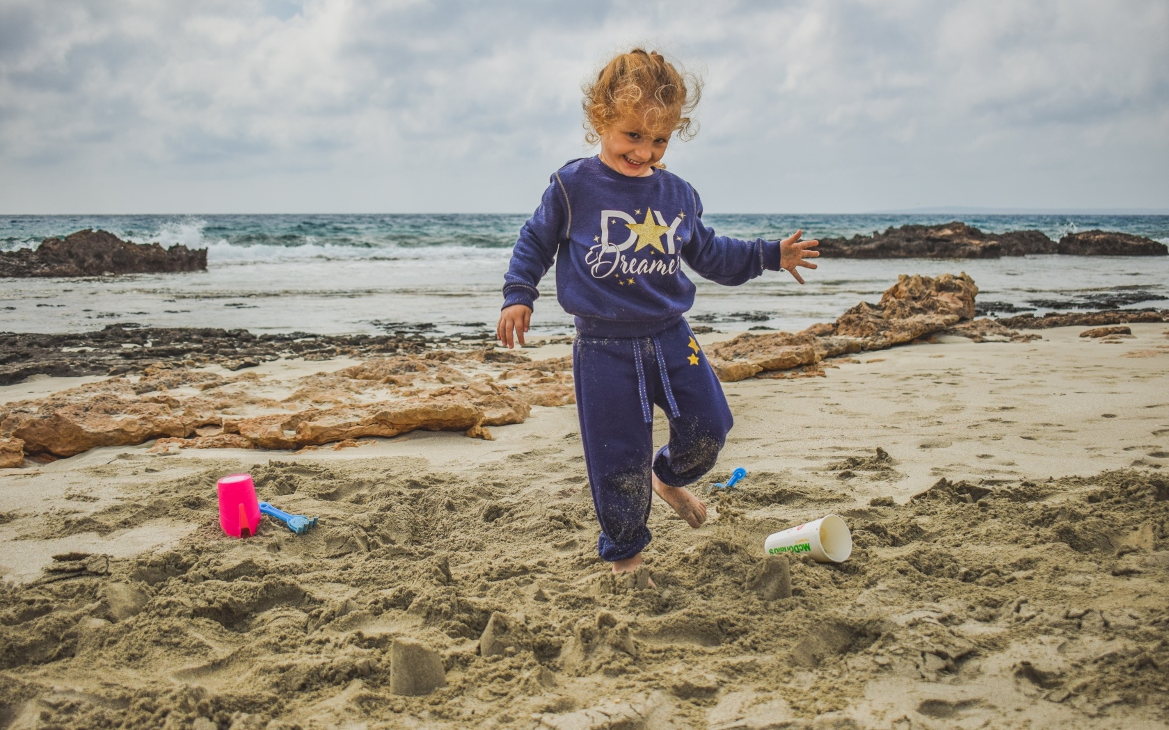 Веселая девочка играет на песке на пляже