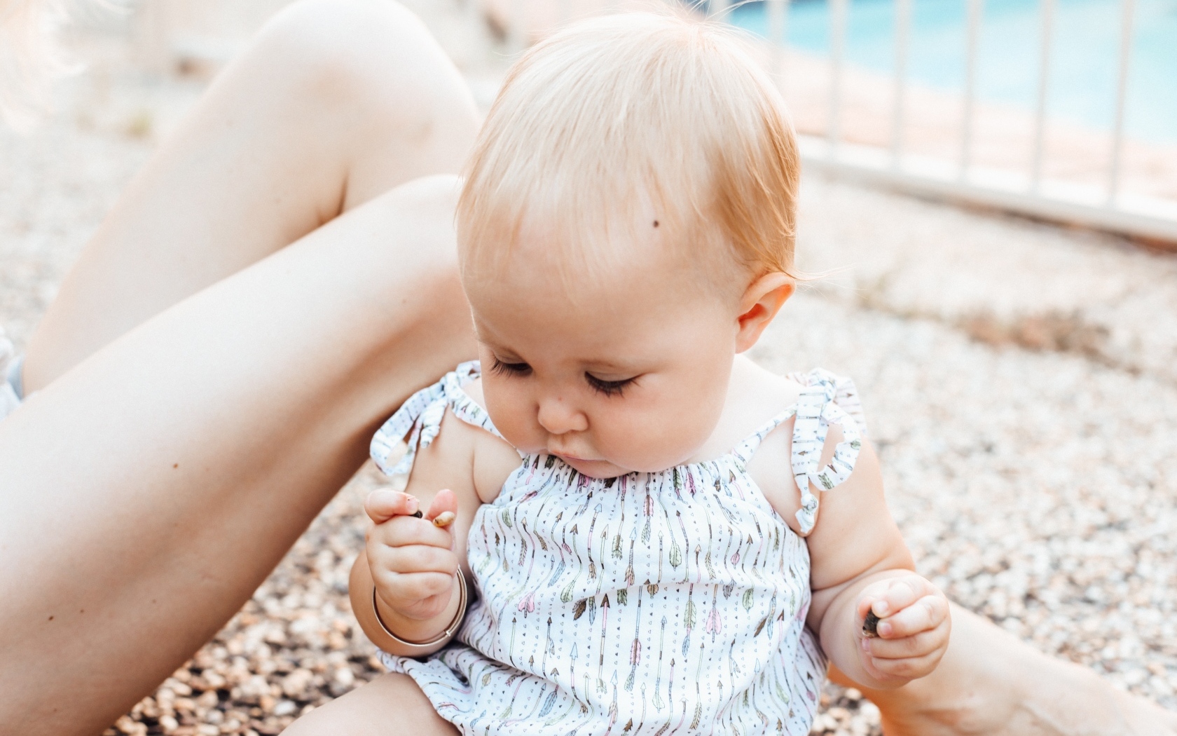 Маленькая светловолосая девочка сидит на песке