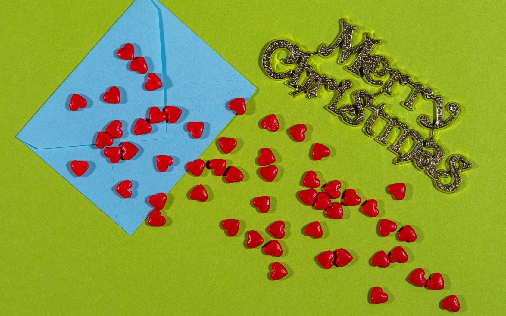 Красные сердечки и голубой конверт на зеленом фоне на Рождество