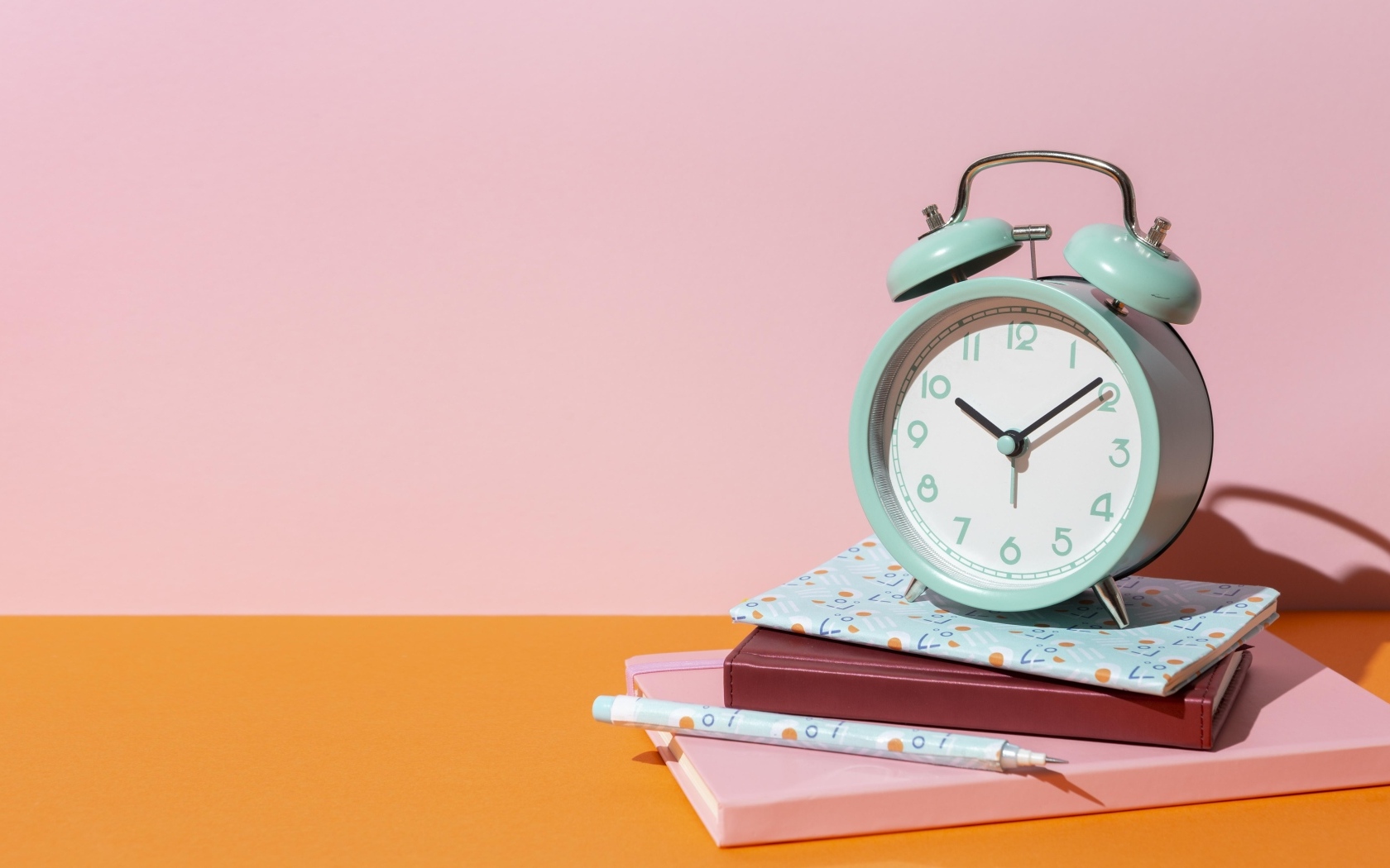 Будильник с книгами на розовом фоне