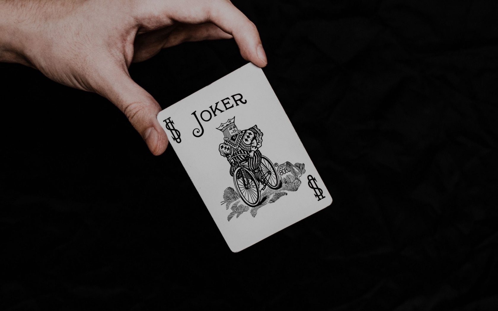 Карта Джокер в руке на черном фоне