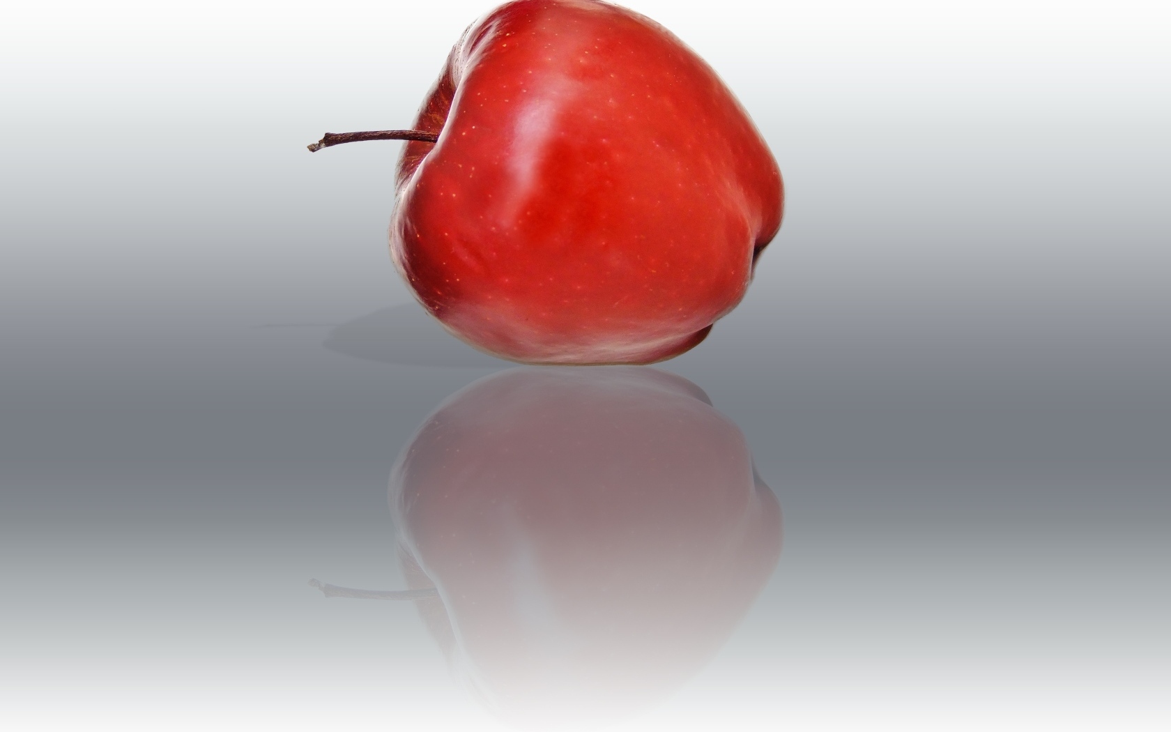Красное яблоко отражается в серой поверхности