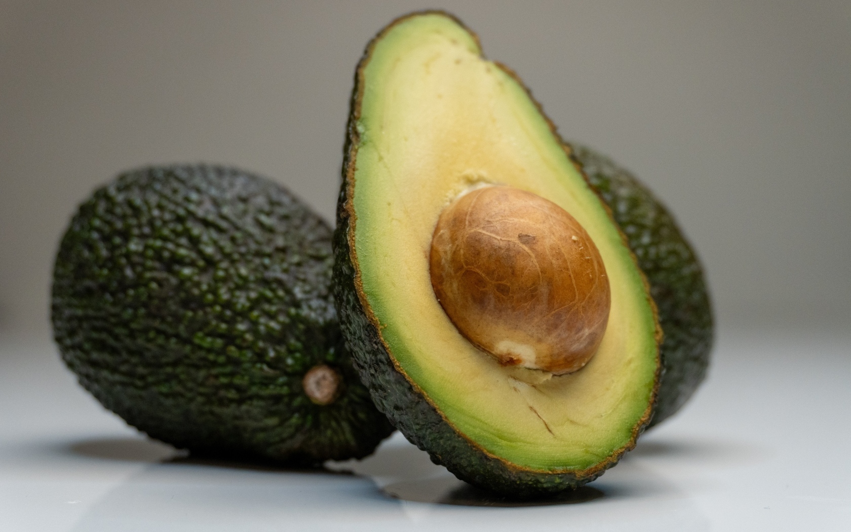 Спелое зеленое авокадо с косточкой на сером фоне
