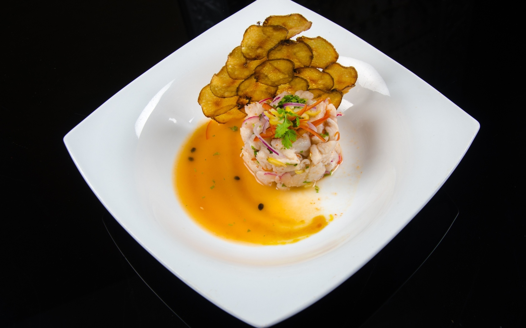 Морепродукты с соусом на большой белой тарелке на черном фоне