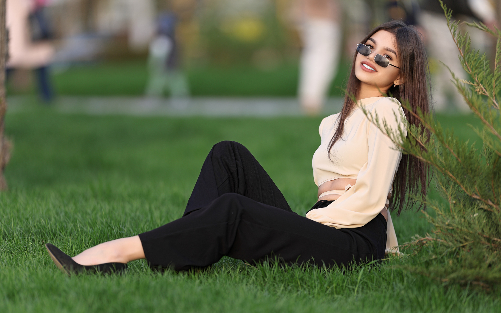Девушка в черных брюках и блузке сидит на траве