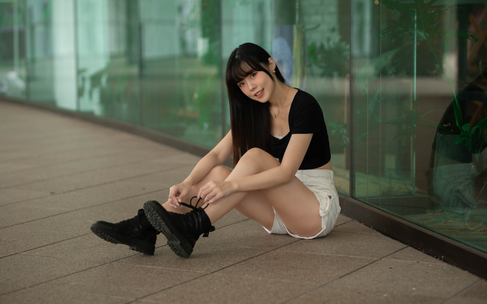 Азиатка в шортах сидит у стеклянной стены