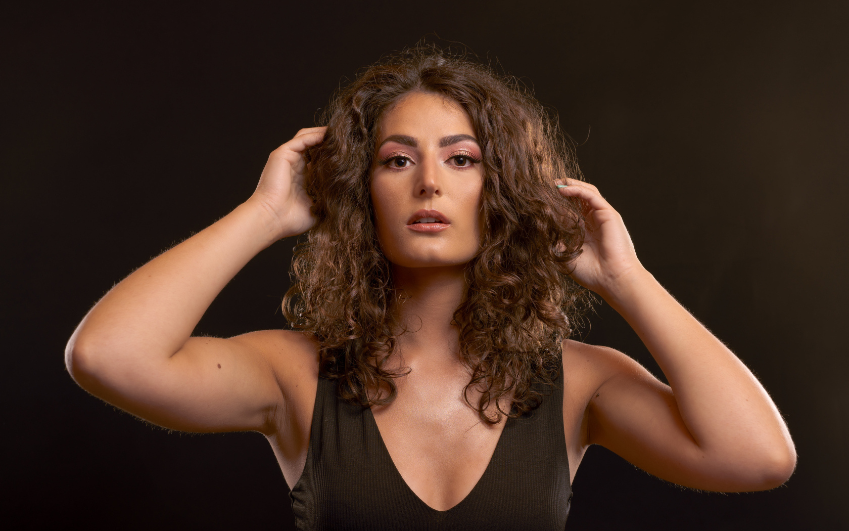 Кудрявая девушка держит руки в волосах на черном фоне