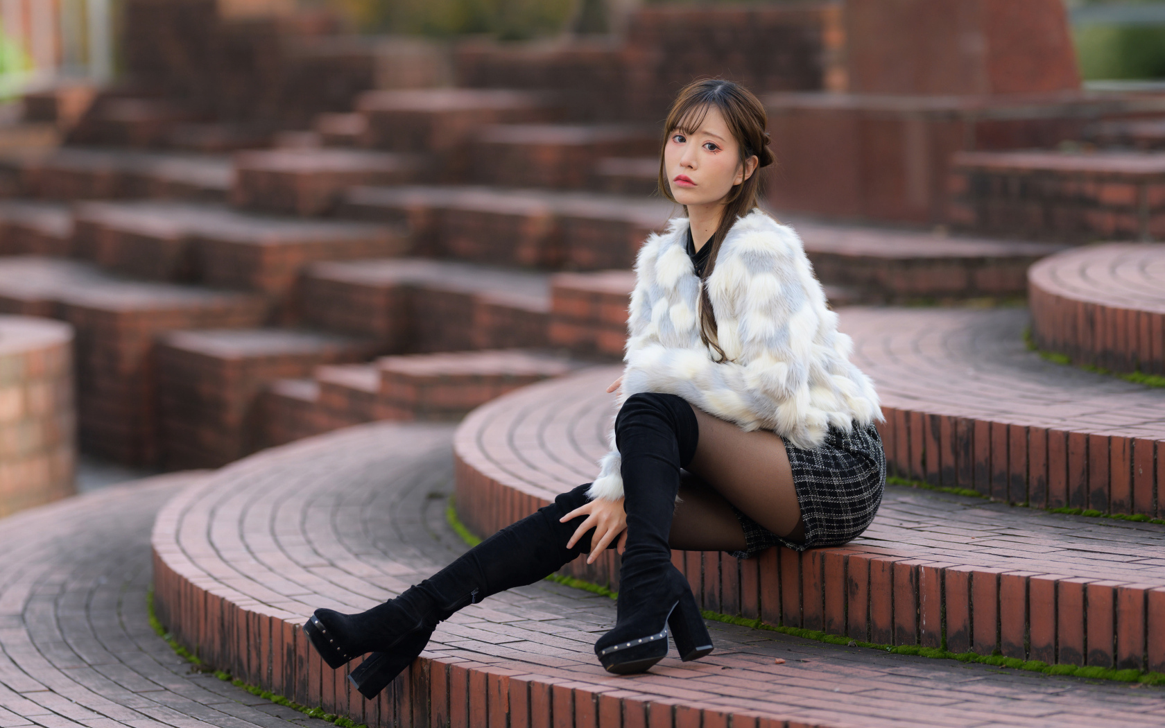 Грустная азиатка в шубе сидит на ступеньках