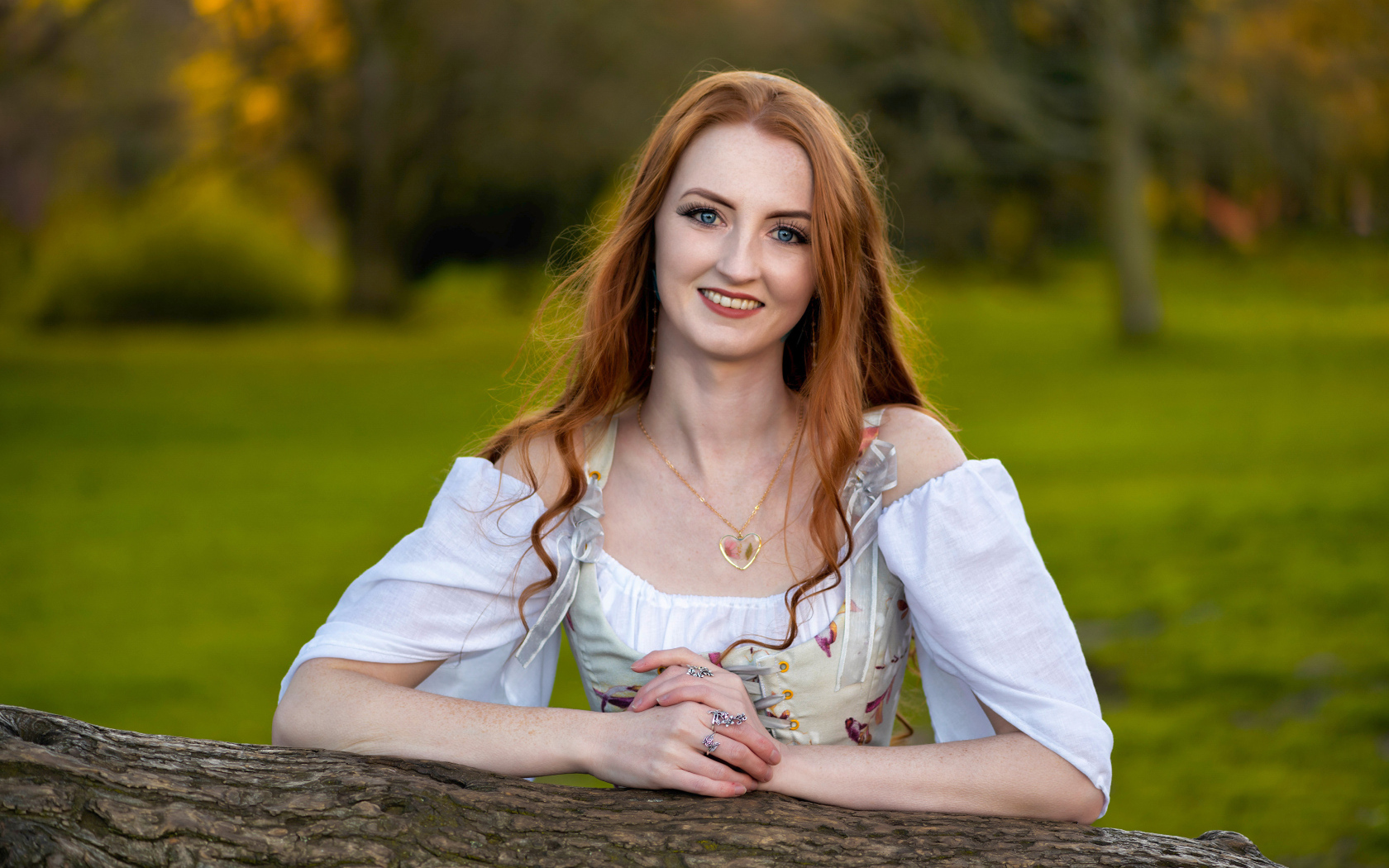 Улыбающаяся рыжеволосая девушка стоит у дерева