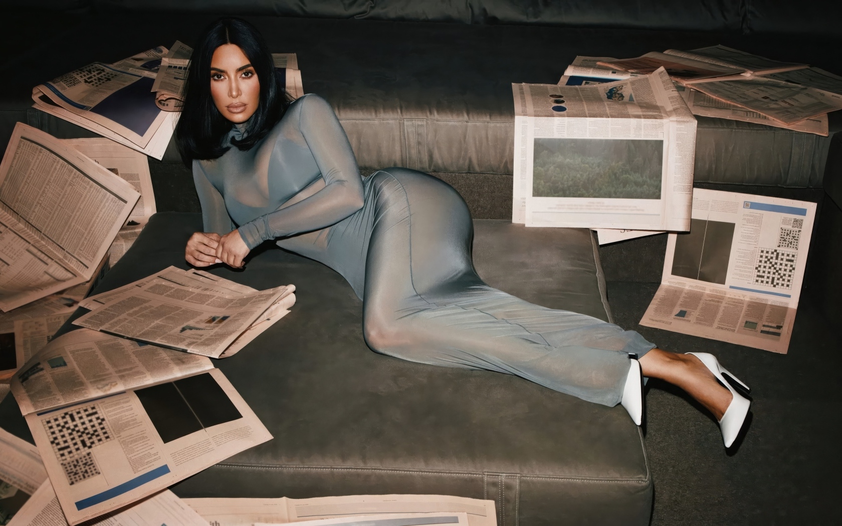 Модель Ким Кардашьян лежит на диване с газетами