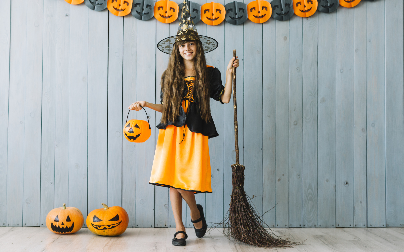 Девочка в костюме ведьмы у стены с декором на Хэллоуин