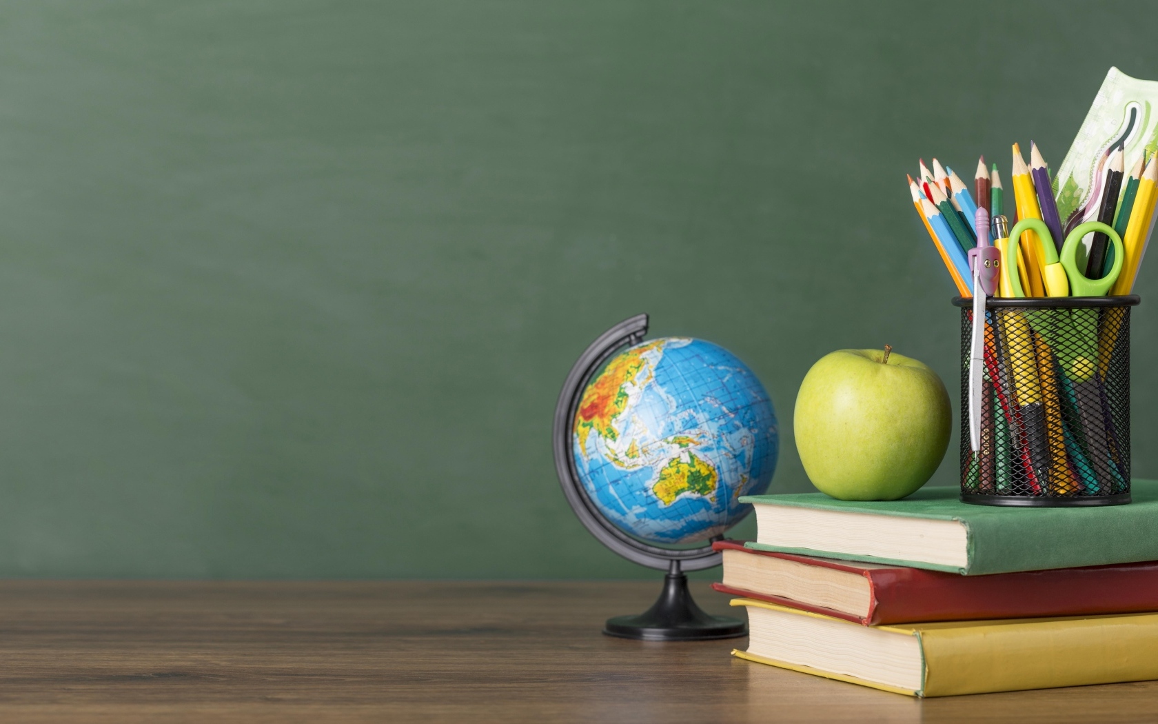 Книги на столе с глобусом, яблоком и ручками в школе