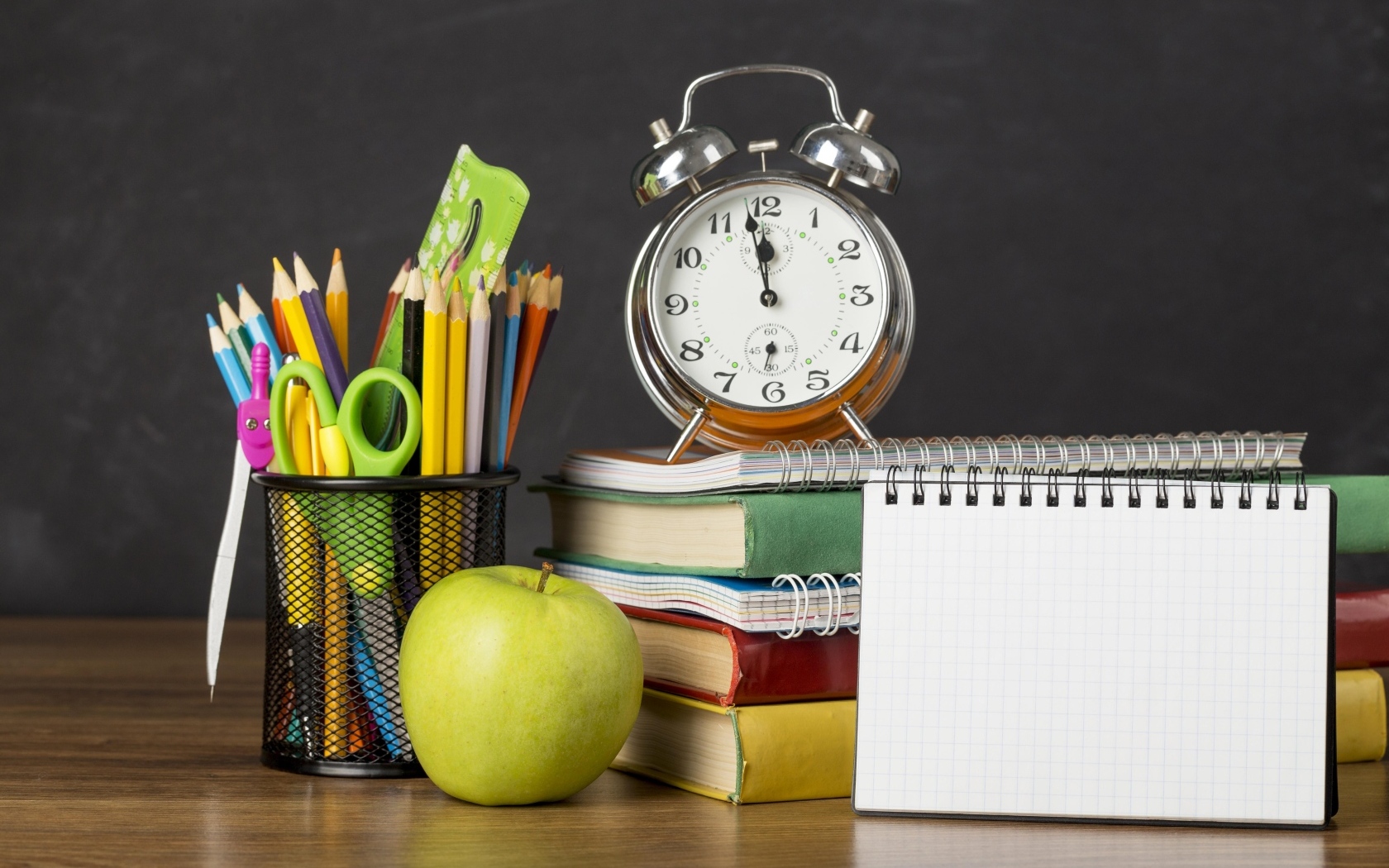 Канцелярские предметы на столе с будильником и книгами 