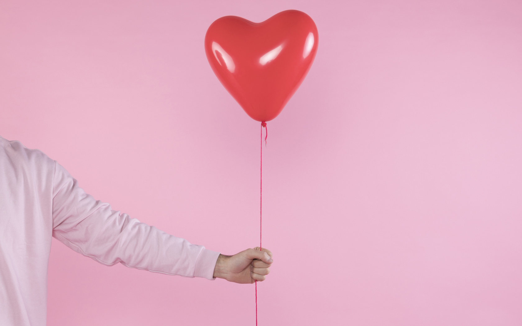 Шарик в форме сердца в руке на розовом фоне