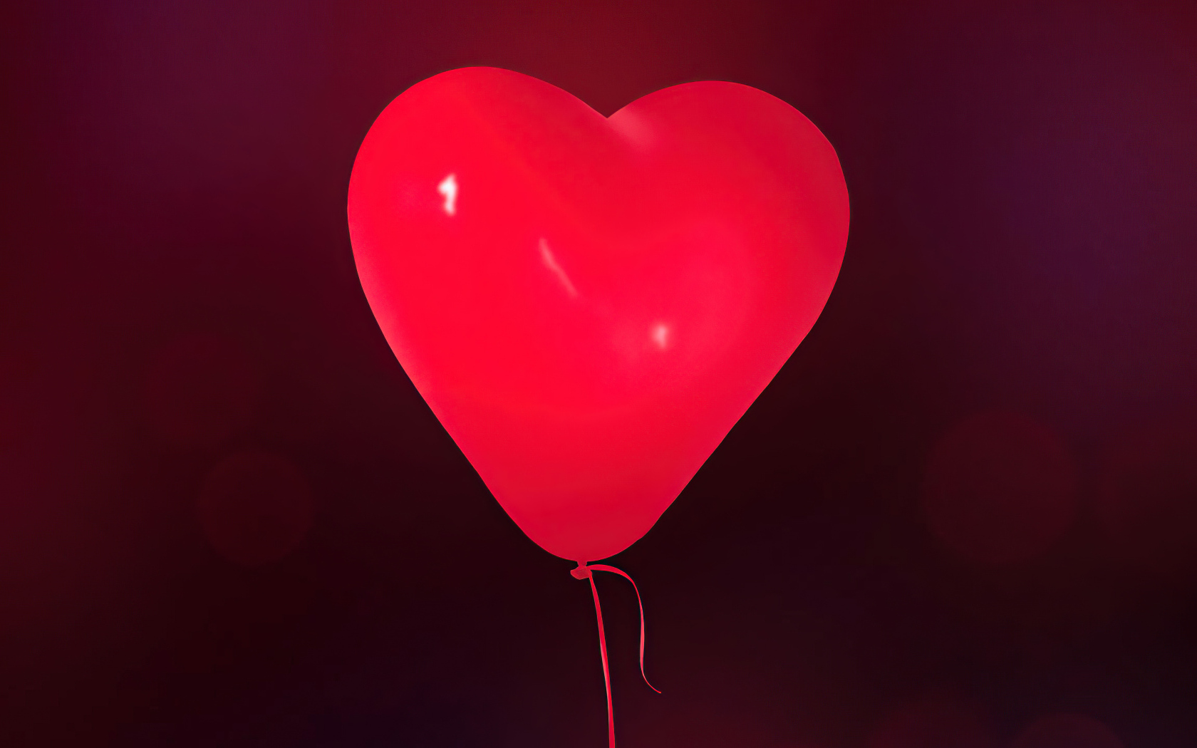 Красный шарик в форме сердца на фоне стены