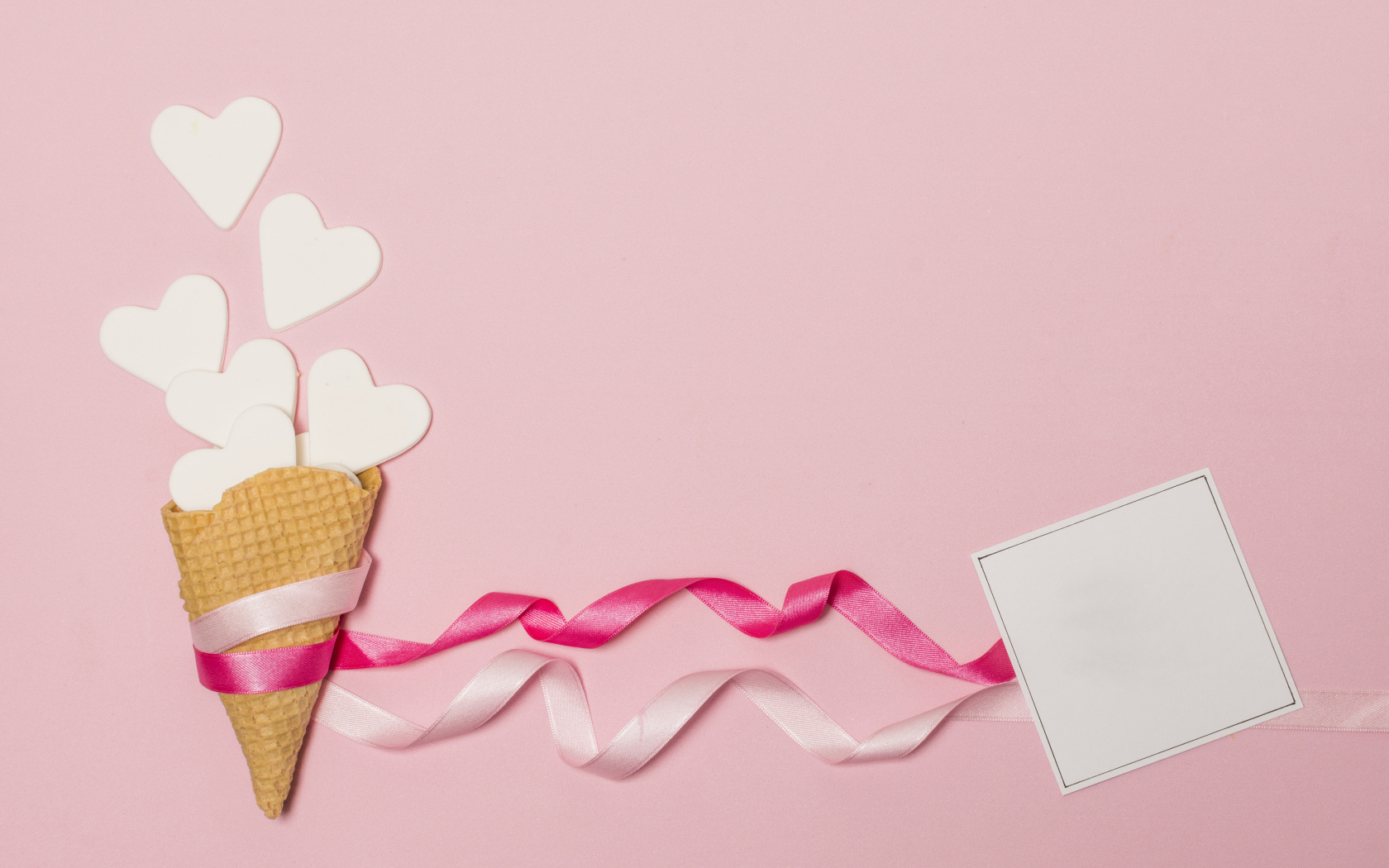 Вафельный рожок с сердечками, лентами и листом бумаги на розовом фоне