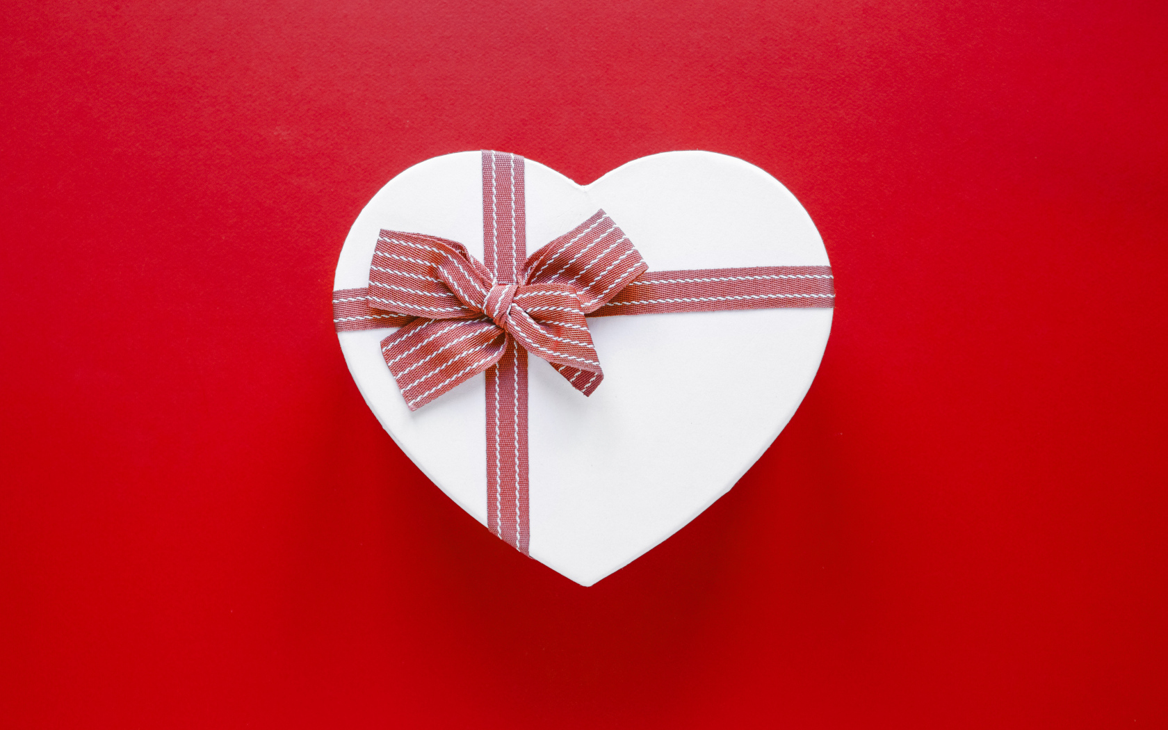 Белая коробка в форме сердца с бантом на красном фоне