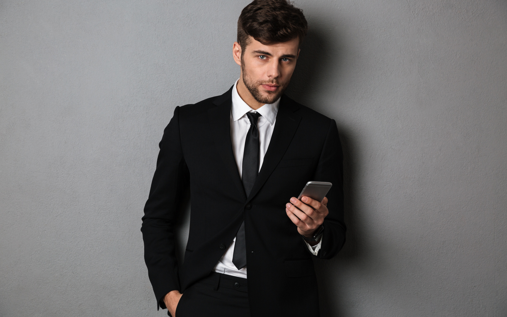Деловой мужчина в костюме стоит у стены с телефоном