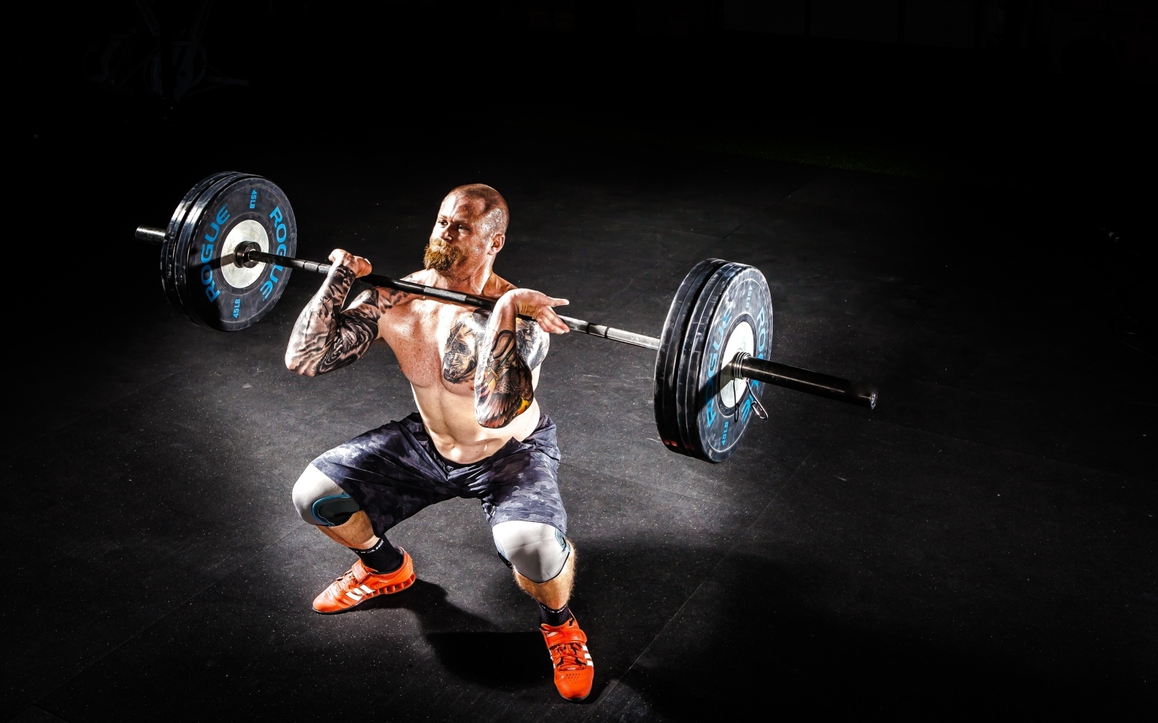 Сильный мужчина с татуировками на теле поднимает штангу