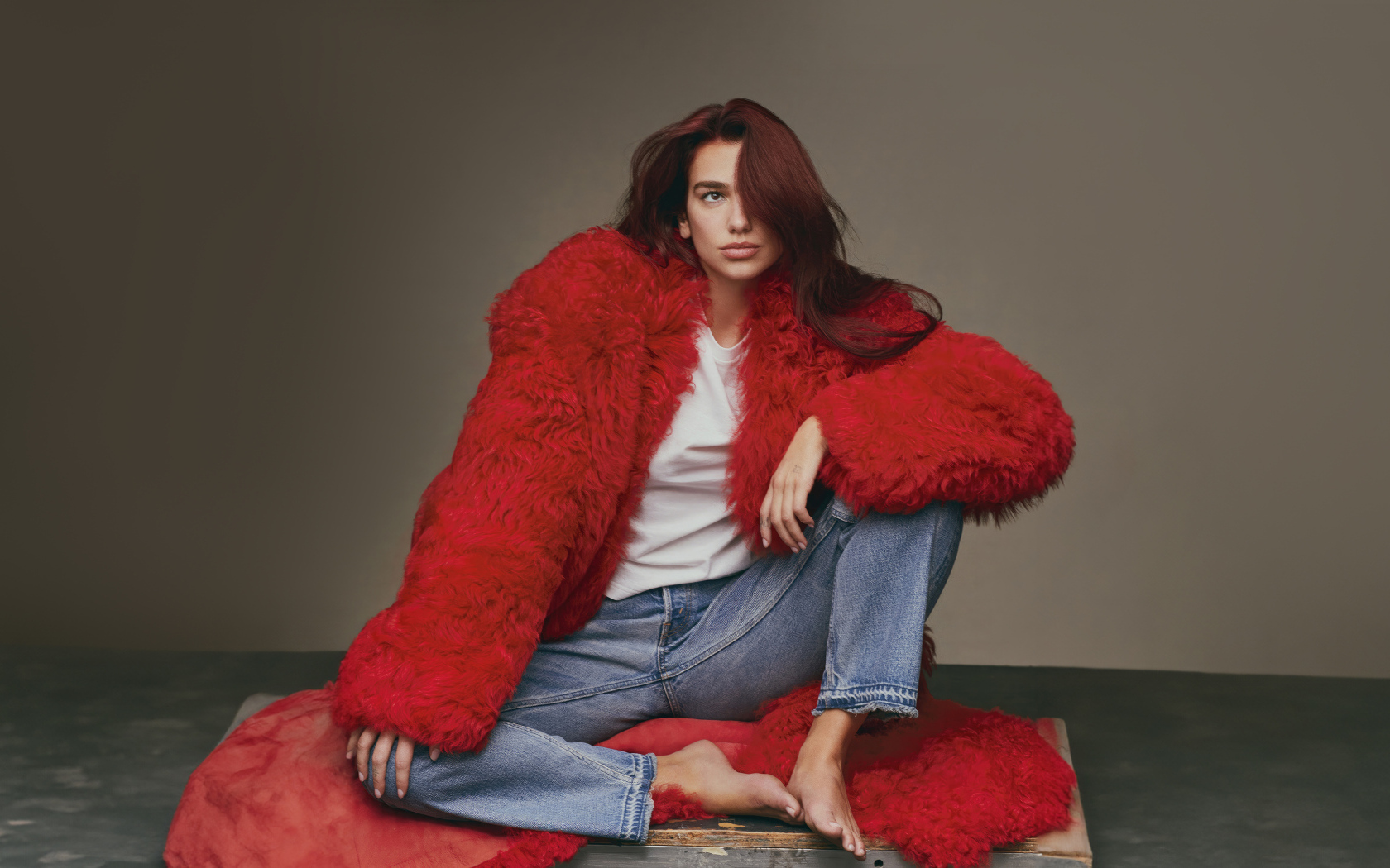 Певица Дуа Липа в красной шубе сидит на полу