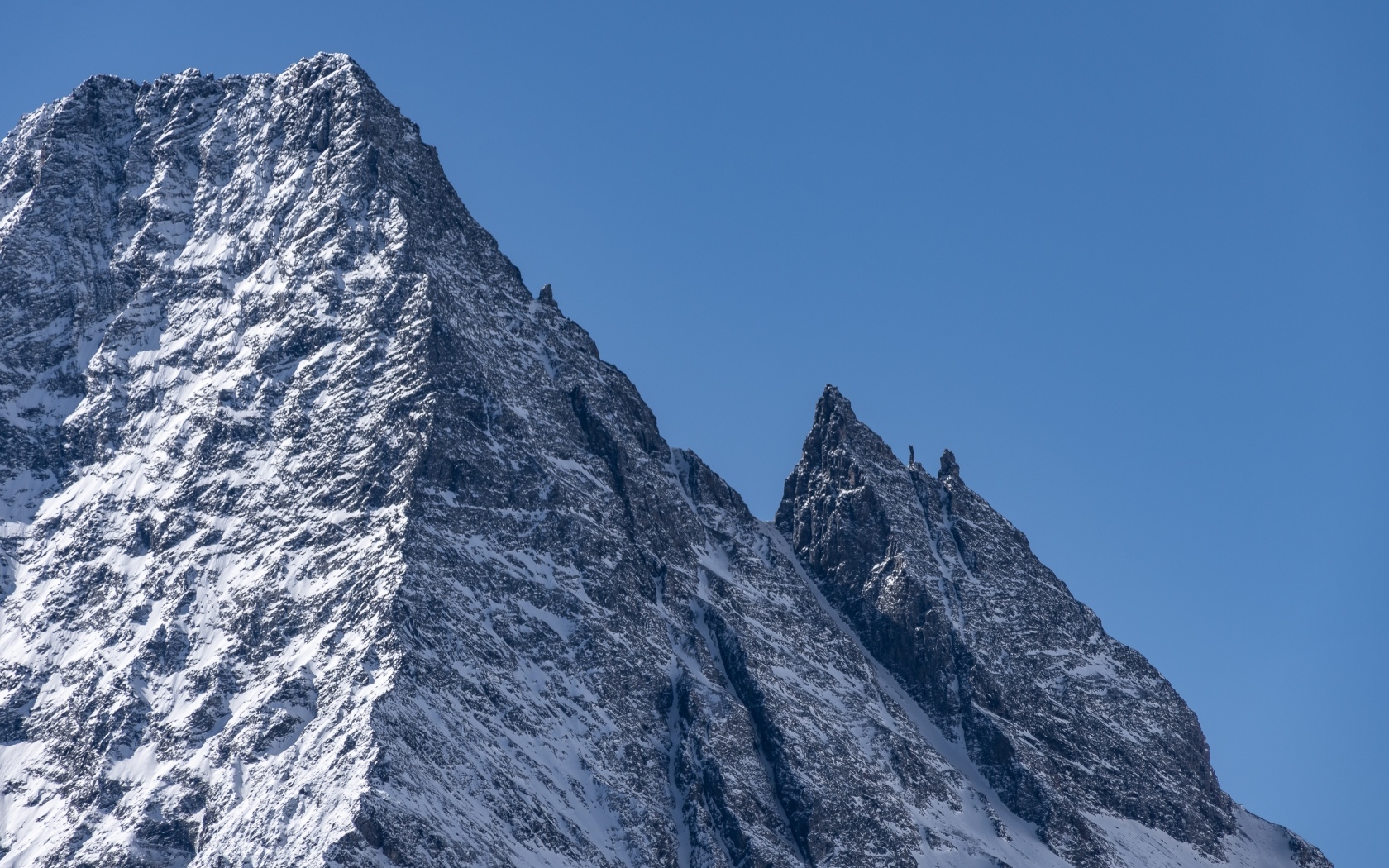 Крутая вершина горы в снегу на фоне голубого неба