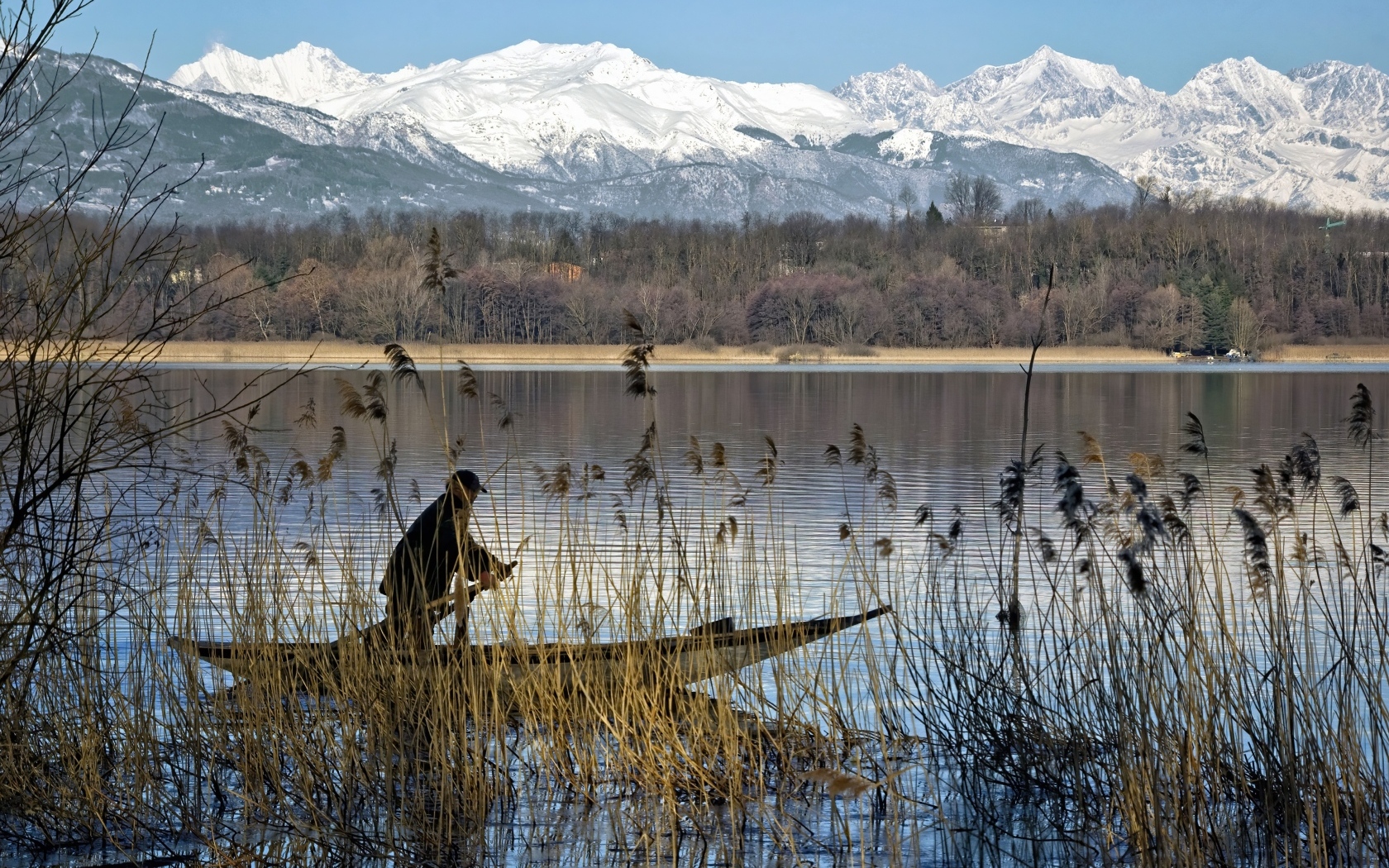 Рыбак плывет по воде на фоне заснеженных гор