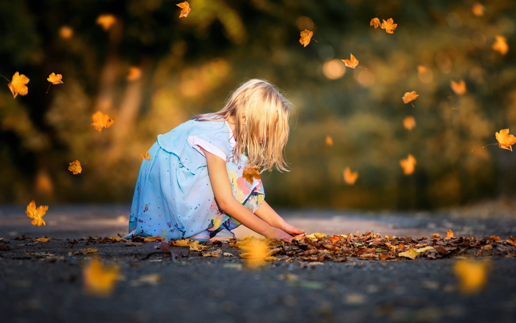Девочка в платье играет с листьями на дороге