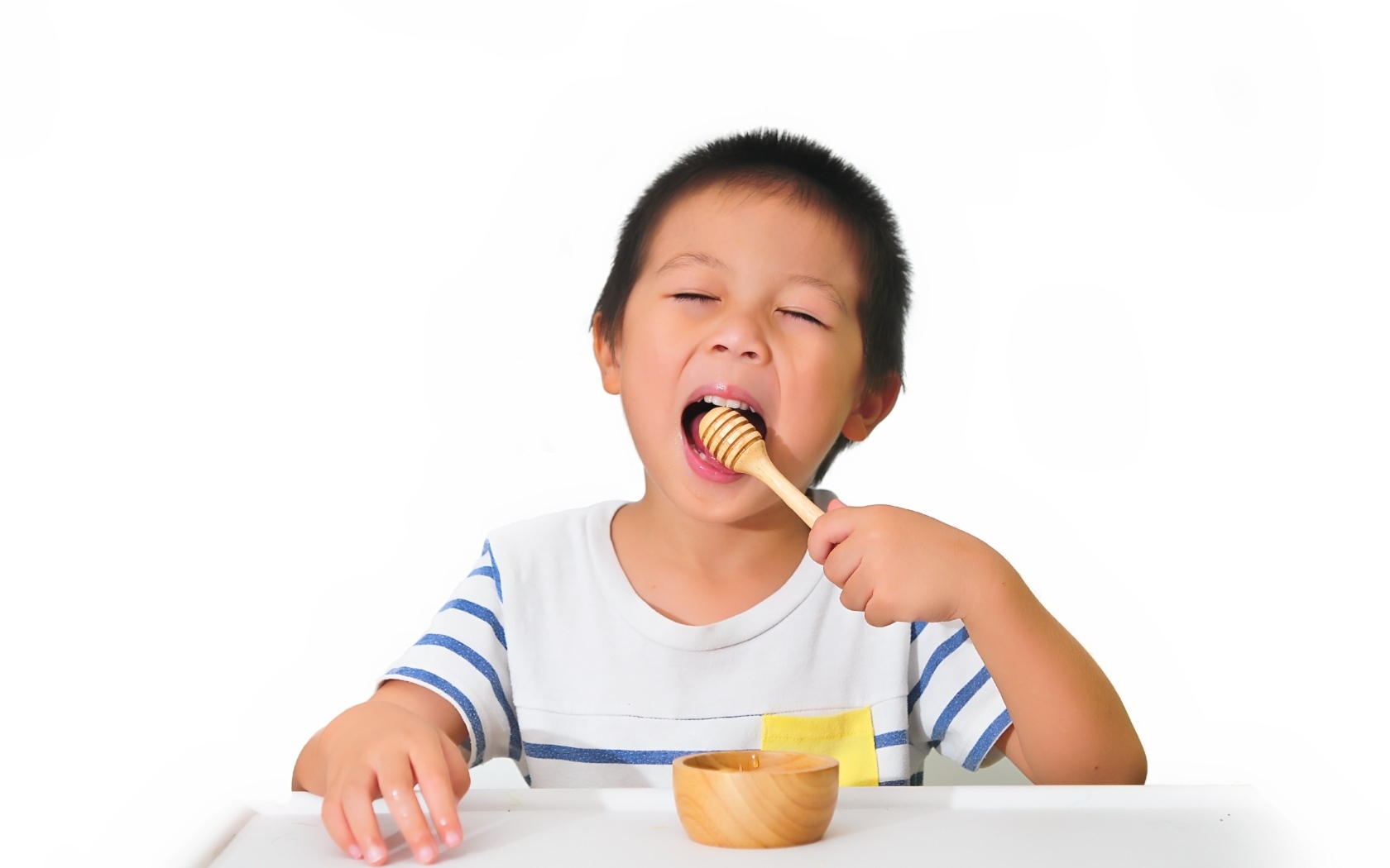Маленький мальчик ест мед на белом фоне