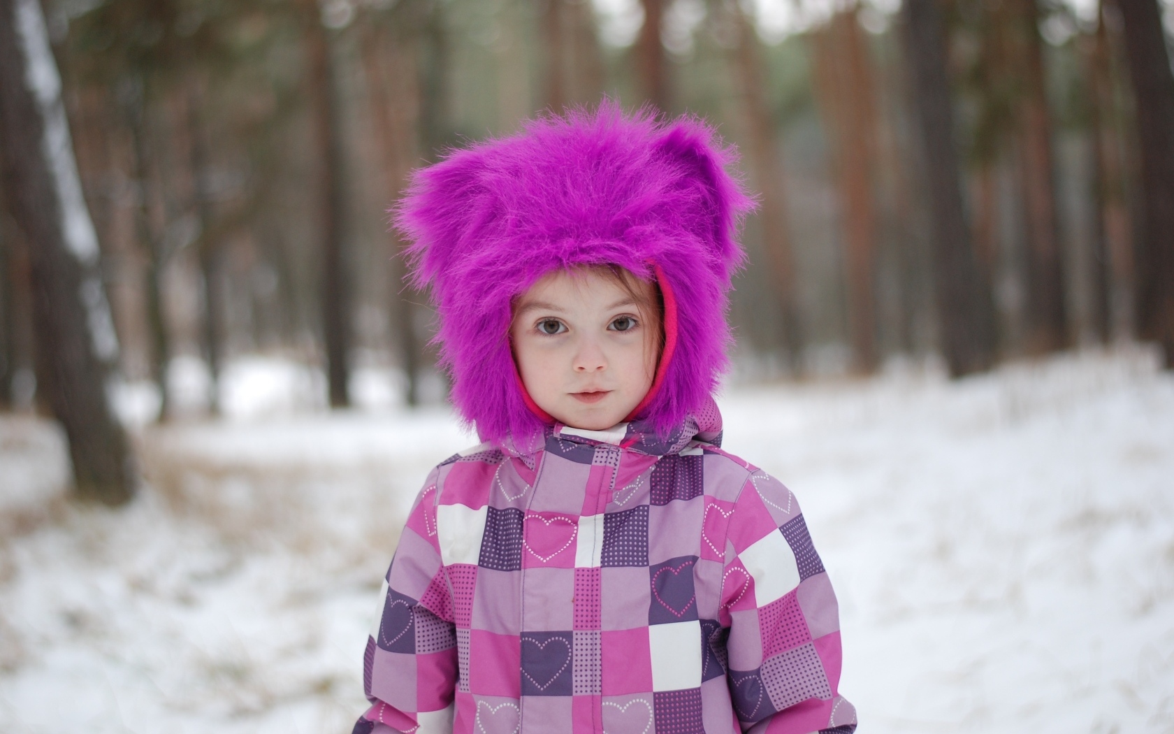 Маленькая девочка в меховой шапке в лесу зимой