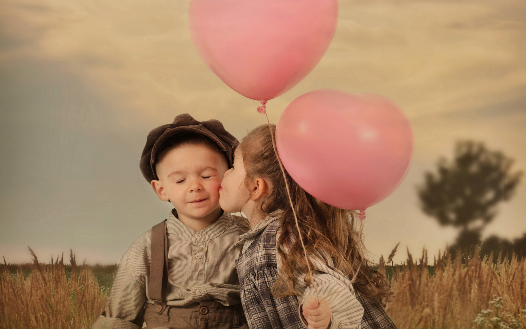 Маленькая девочка с шариками целует мальчика