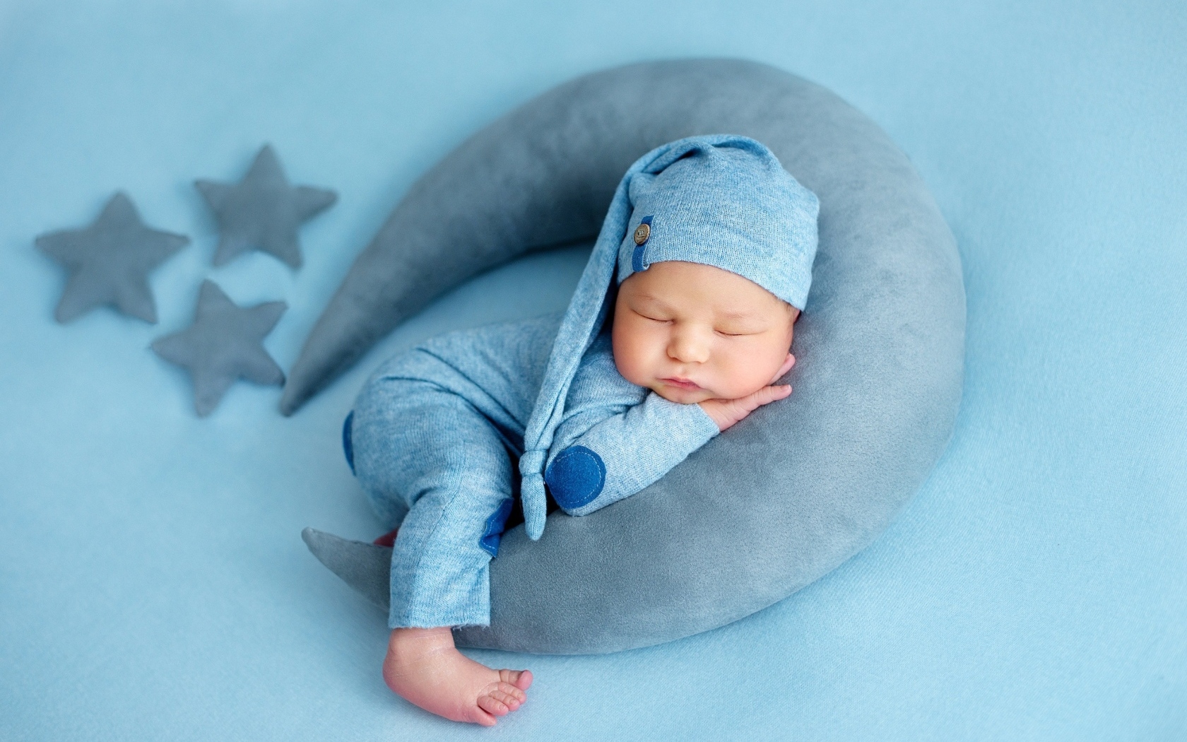 Новорожденный малыш спит на игрушечном полумесяце на голубом фоне